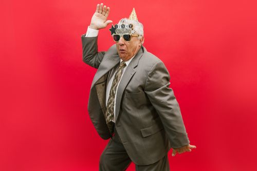 Free Senior man joyfully celebrating his birthday in a gray suit against a vibrant red background. Stock Photo