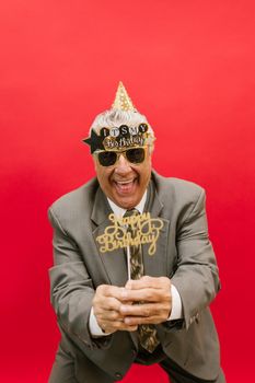 Elderly man in gray suit celebrating his birthday with cheerful spirit and props.