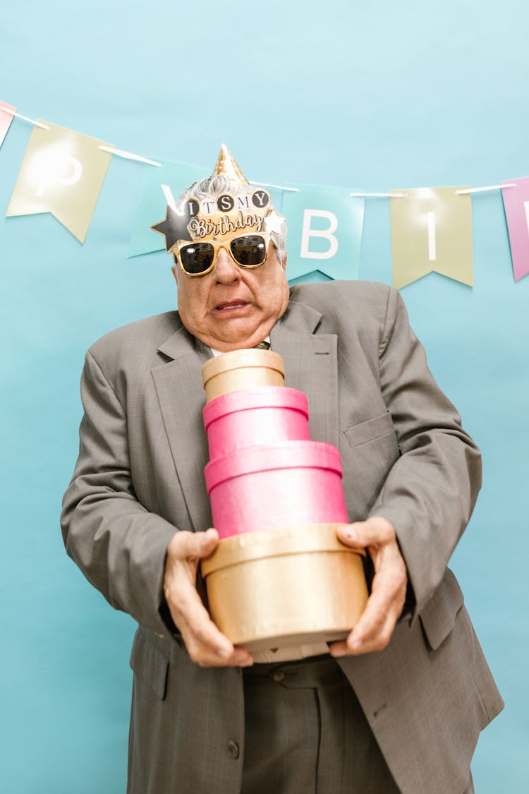 An Elderly Man Holding A Stack Of Gift Boxes