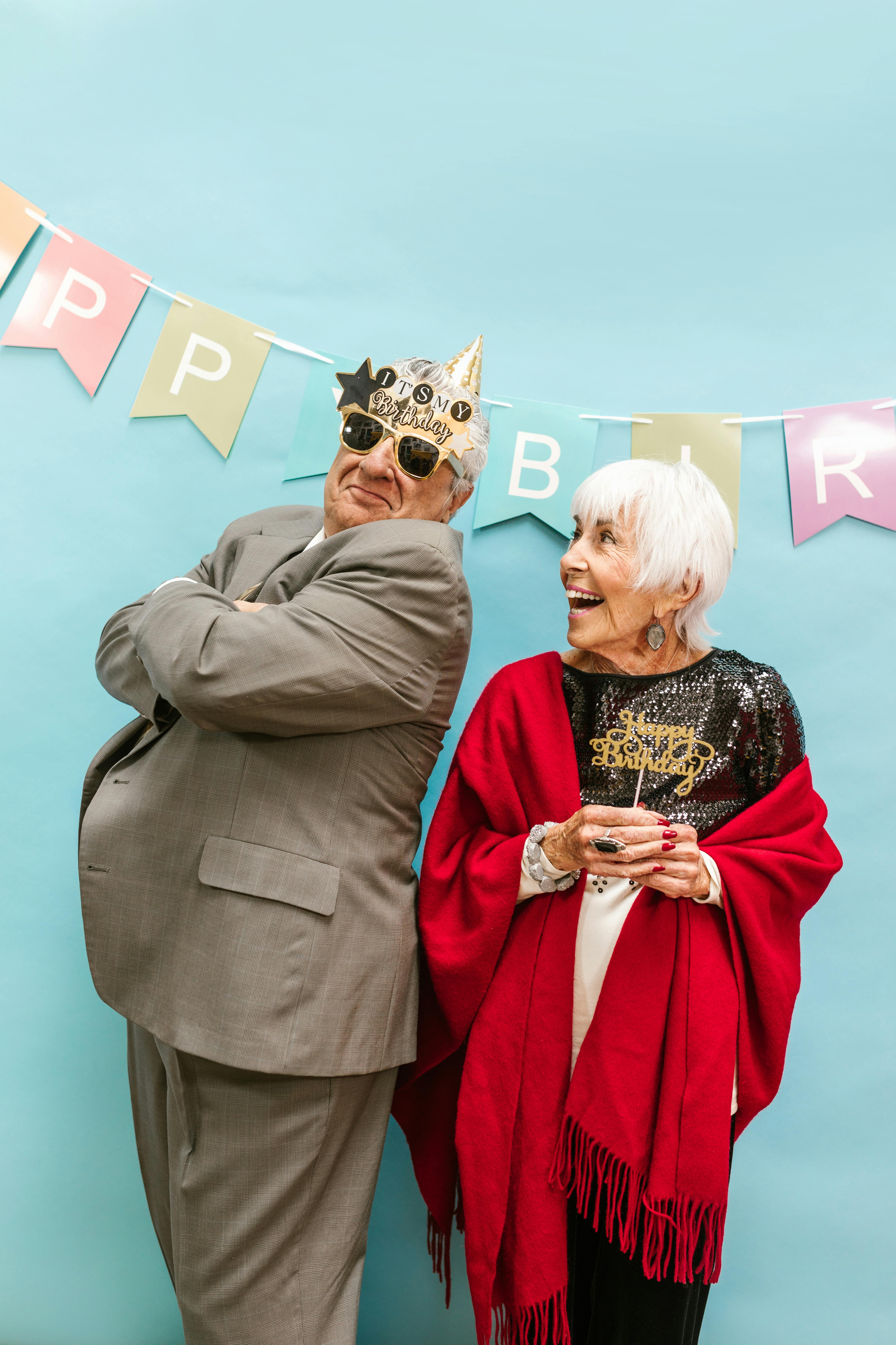 Elderly couple in festive attire celebrating a joyful birthday with laughter.