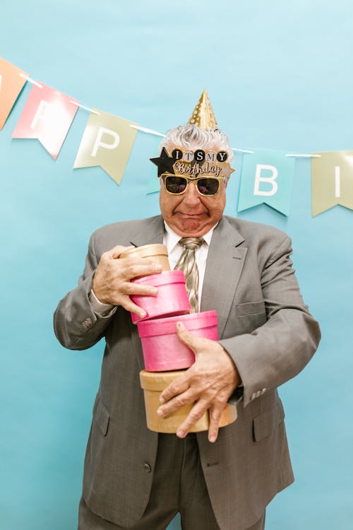 Man in Gray Suit Holding Pink and Gold Gift Box