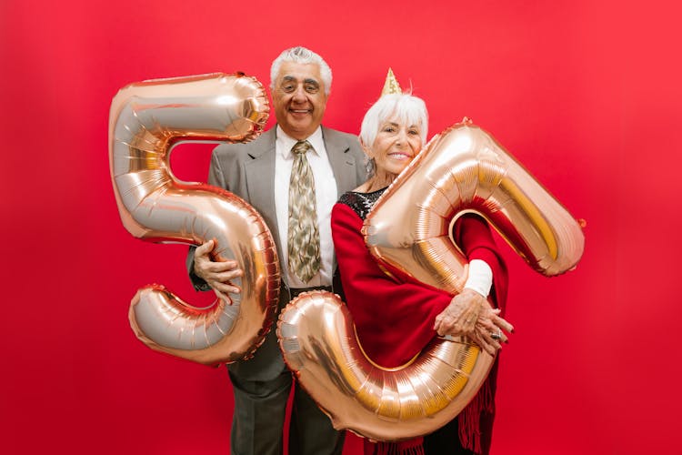 An Elderly Man And Woman Holding Number Balloons 