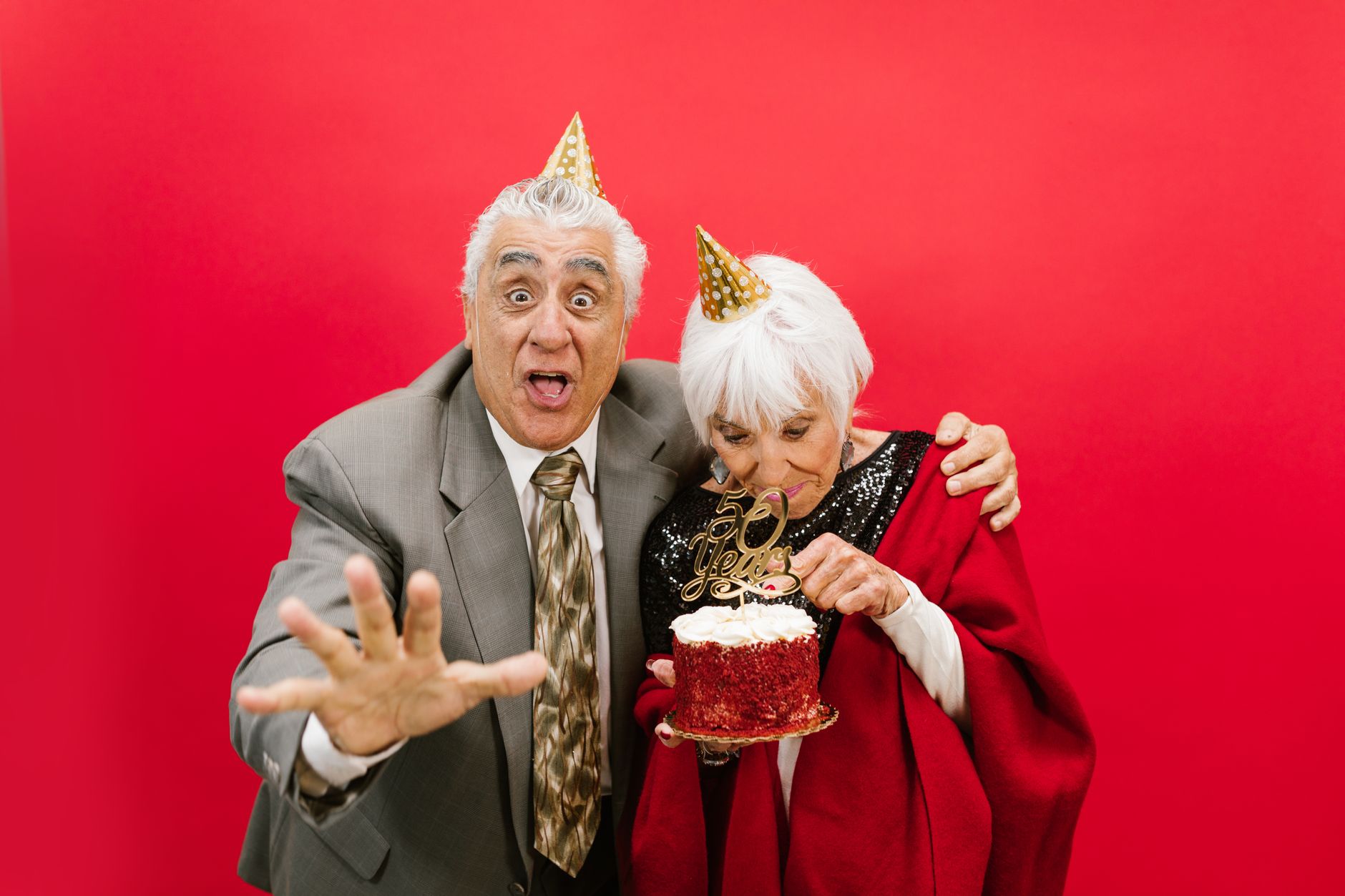 Joyful elderly couple celebrating their 50th anniversary with a cake and party hats in a festive setting.