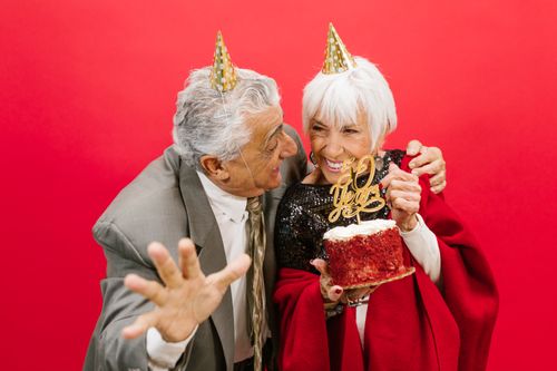 Free Elderly couple with party hats celebrating 50th anniversary with a cake and laughter. Stock Photo