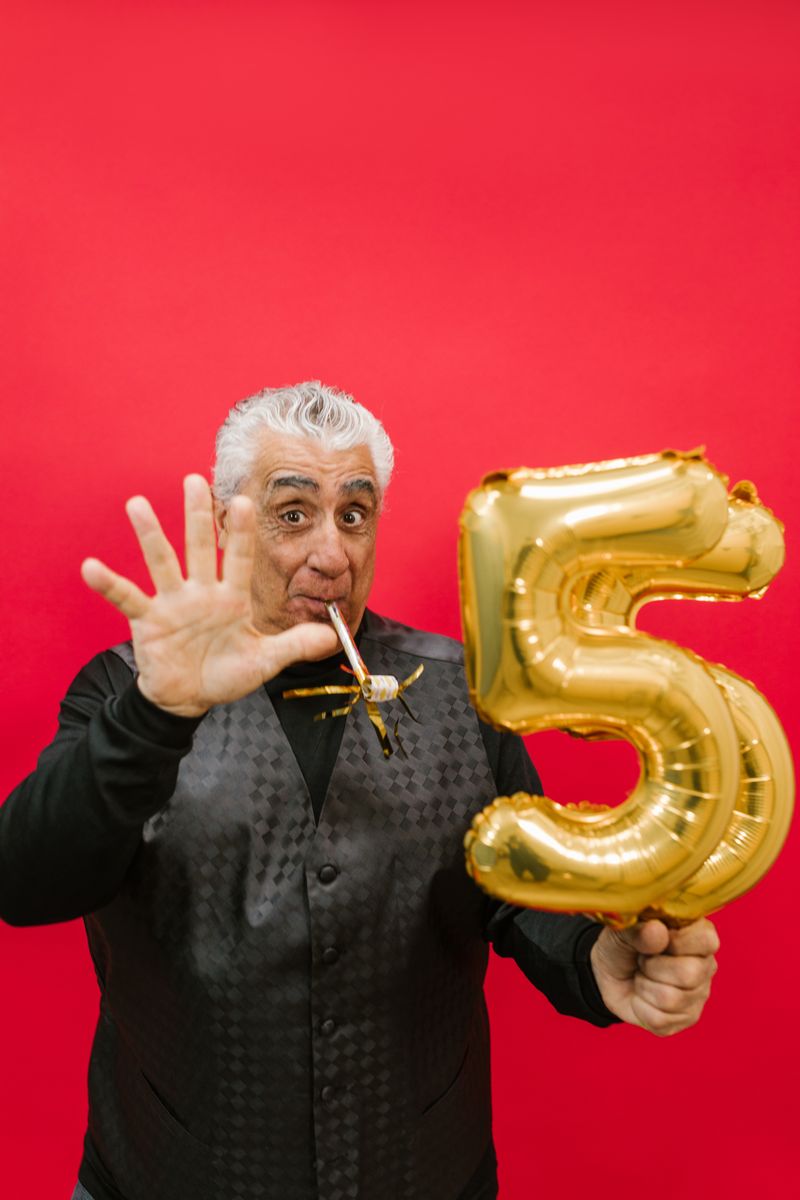 Older man smiling and holding number balloons at his birthday