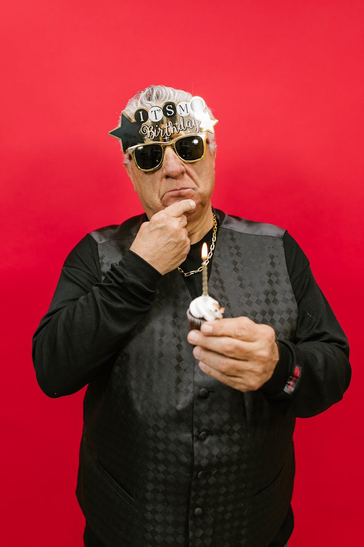 Man In Black Long Sleeves And Vest Holding A Cupcake 