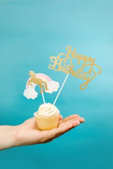 A cupcake with unicorn and Happy Birthday decorations on a baby blue background.