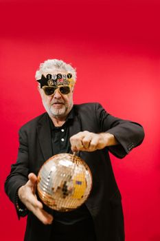Senior adult man in sunglasses celebrating with a disco ball against a red backdrop.