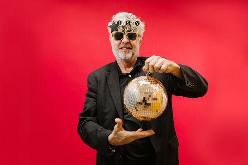 Free A cheerful elderly man with sunglasses and a disco ball against a vivid red background. Stock Photo