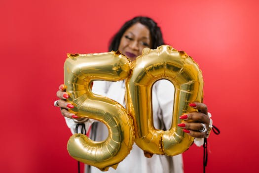 Woman holding gold number 50 balloons on a vibrant red background, symbolizing celebration.