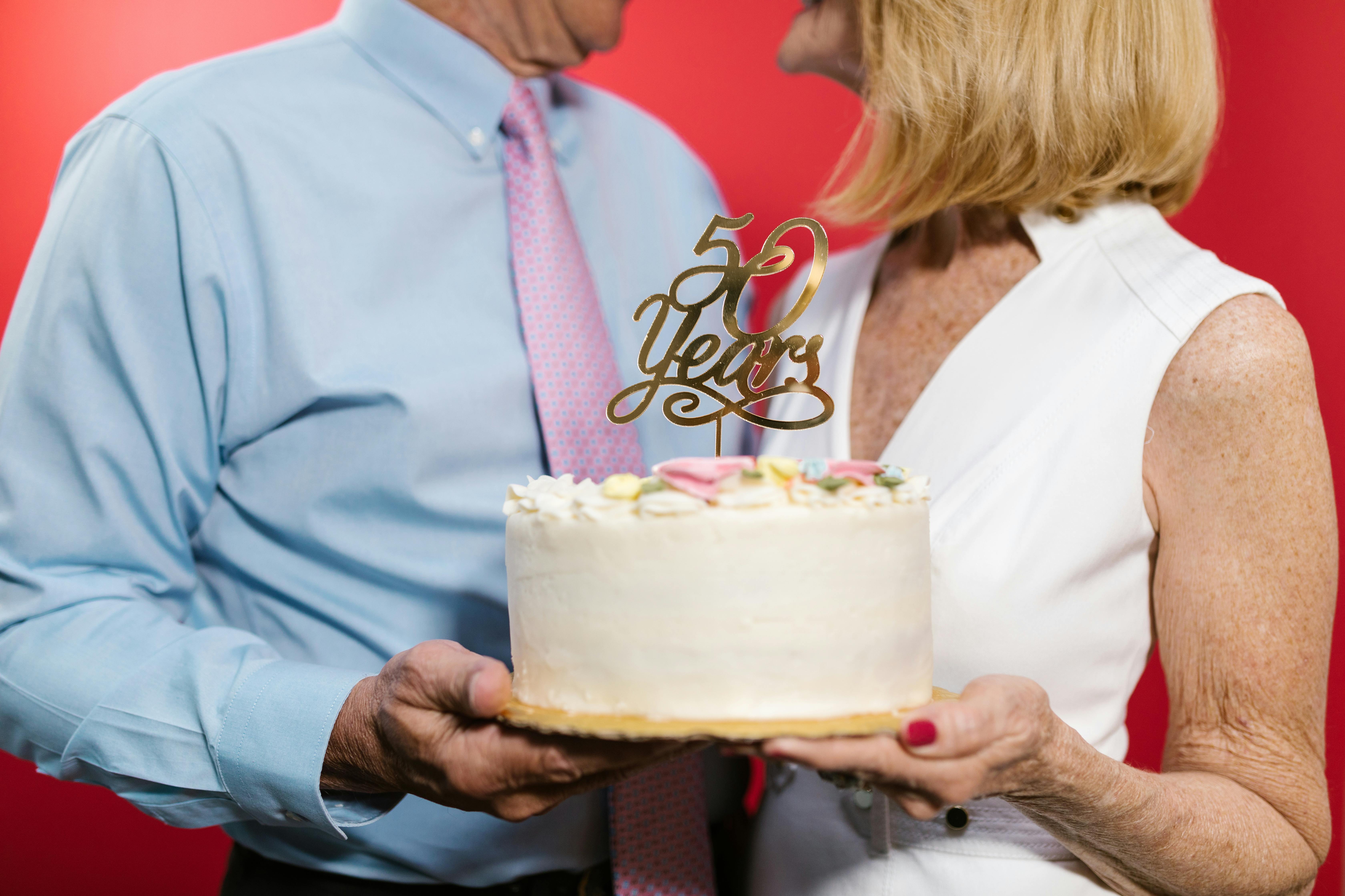 a couple standing next to each other while holding an anniversary cake