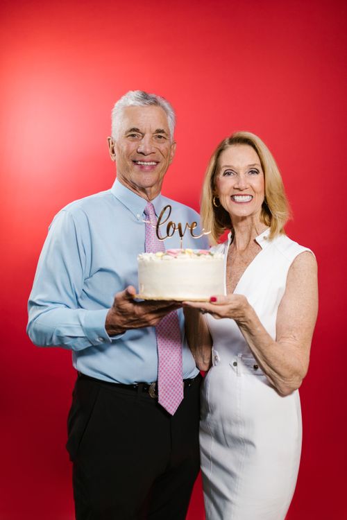 Free Joyful senior couple holding a cake with a love topper against a red background. Stock Photo
