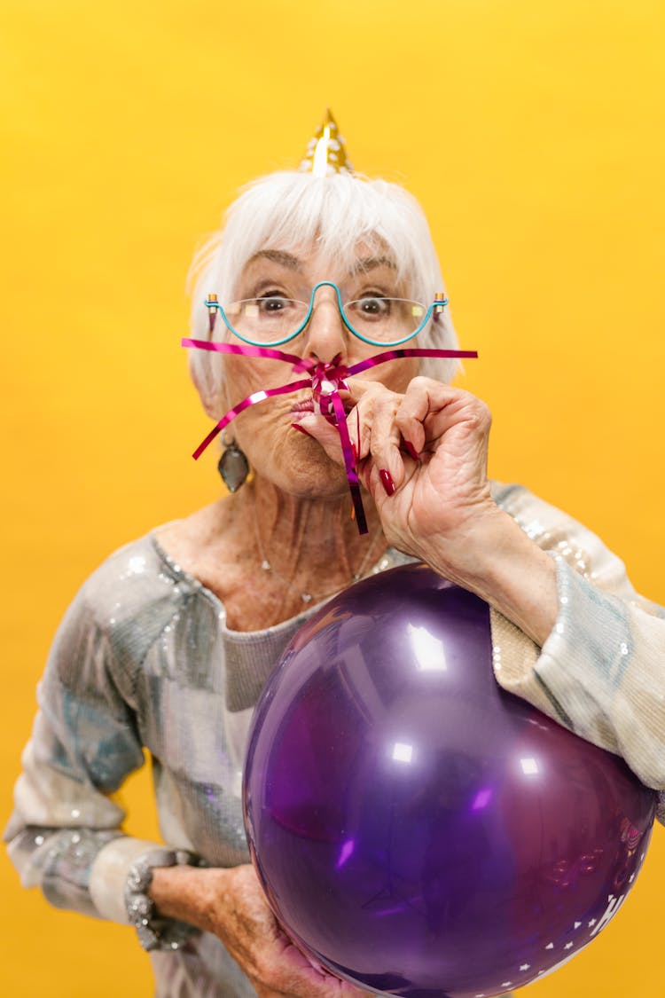 An Elderly Woman With A Party Horn And A Balloon