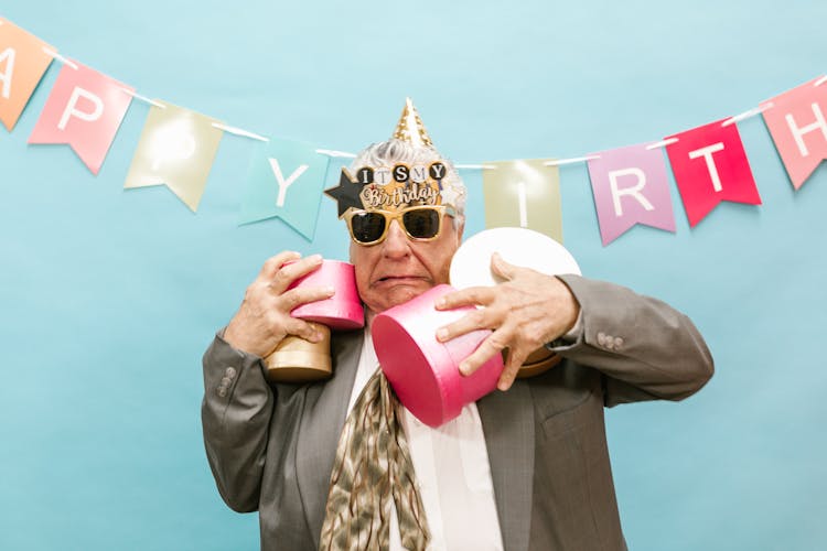 An Elderly Man Wearing Sunglasses And A Party Hat