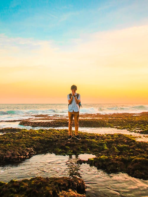 Человек, стоящий на скалах возле пляжа во время золотого часа