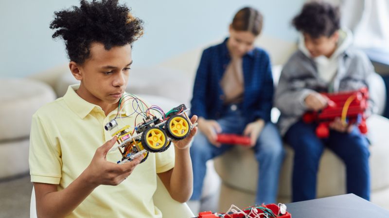 Teenagers building and learning with robotic toy cars indoors, promoting STEM education.