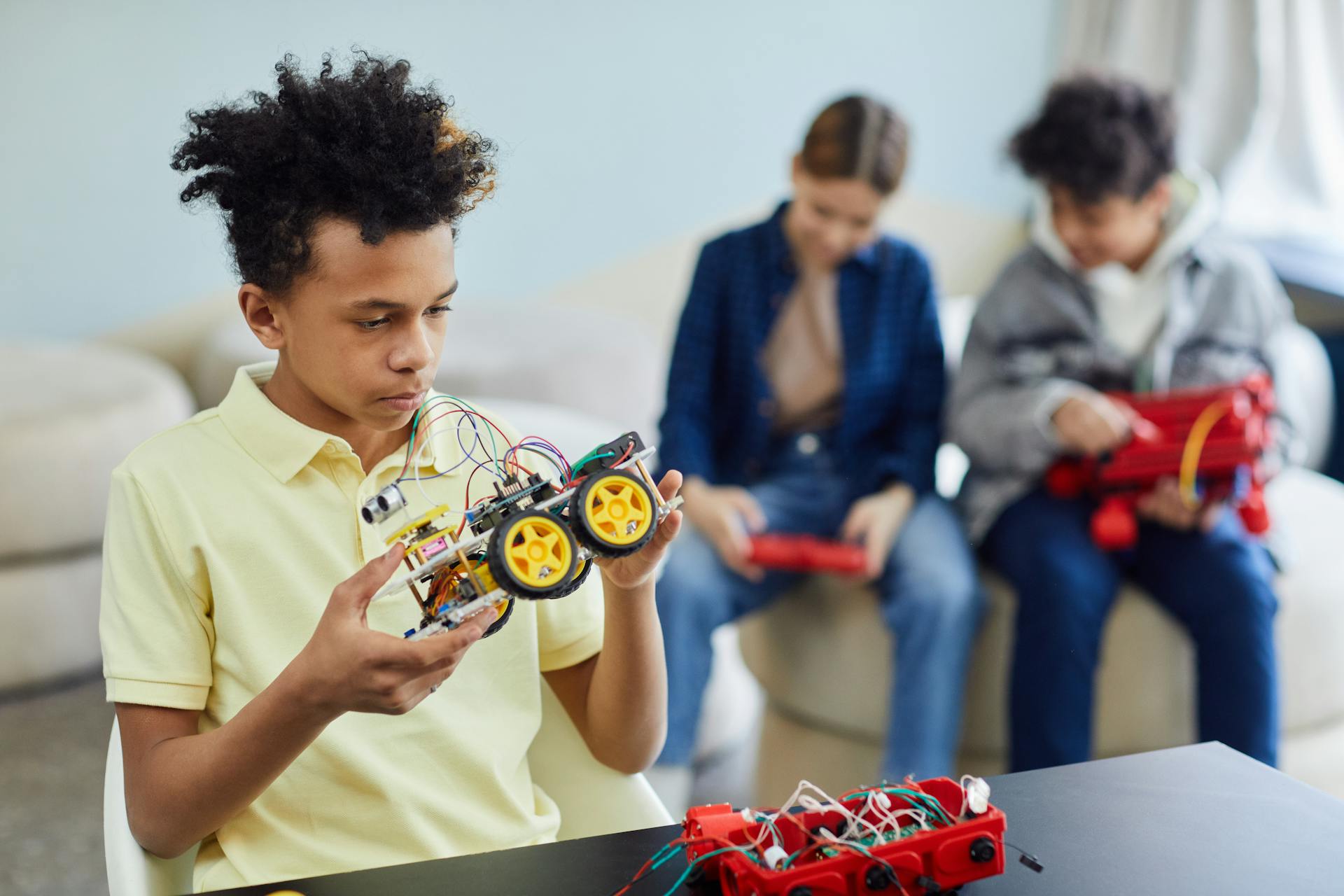 Teenagers building and learning with robotic toy cars indoors, promoting STEM education.