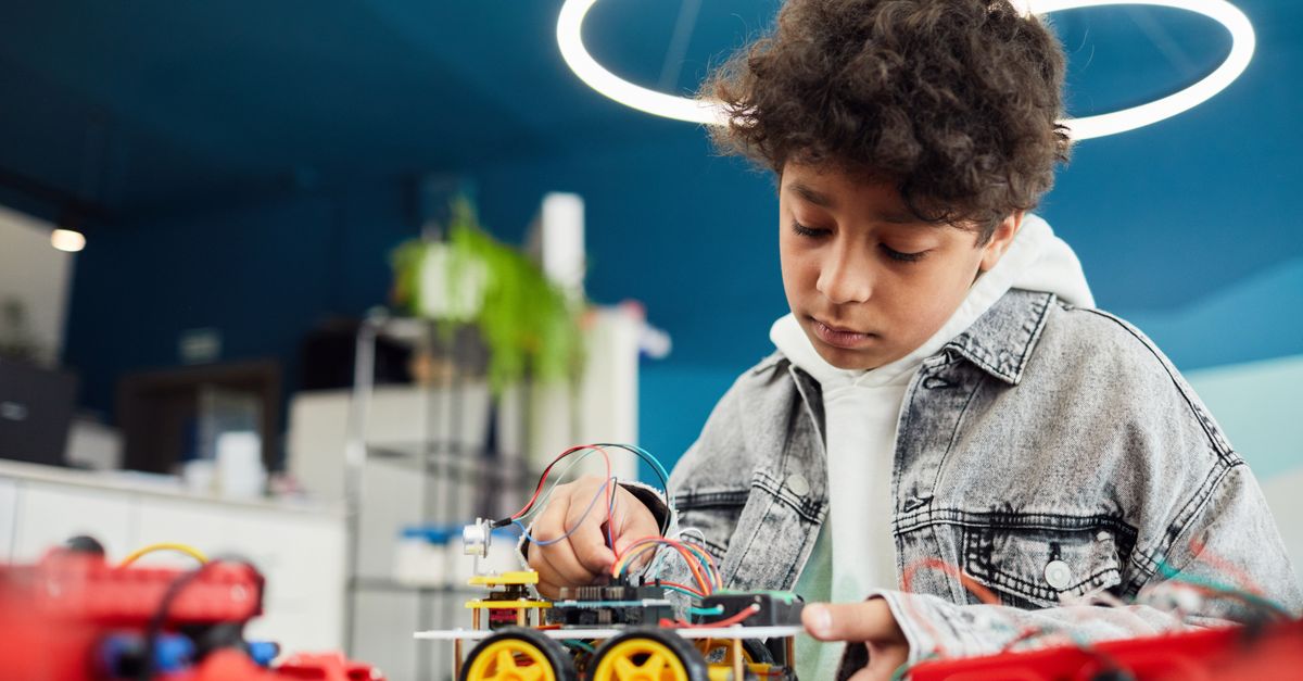 A focused young boy works on a robotics project indoors, showcasing learning and innovation.