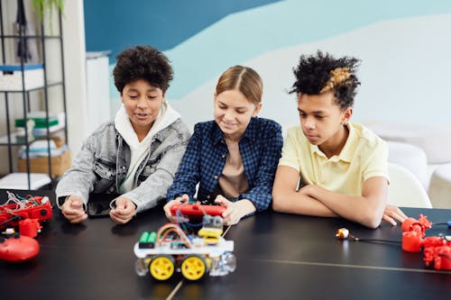 Group of Teenagers Sitting at the Table and Playing with Remotely Controlled Cars 