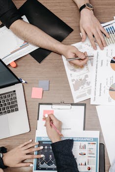 Overhead view of a team collaborating on infographic design with charts and laptops.