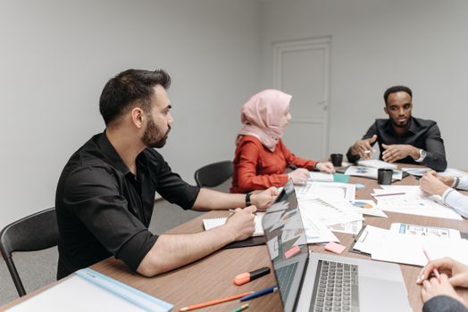 Business team working together at a table, discussing documents and using a laptop.