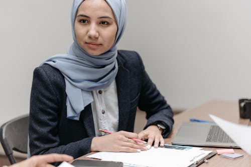 A Woman in Blue Blazer and Hijab Sitting at a Table