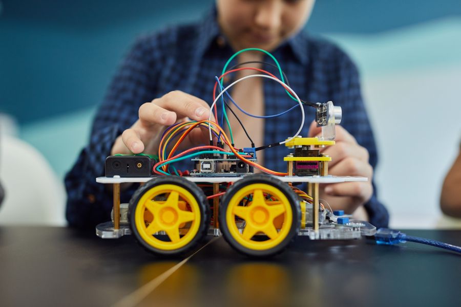 Des mains d'adolescent assemblent un petit robot à roues avec une carte électronique et des câbles