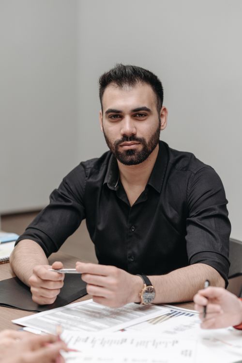 Free A confident businessman with a beard sitting at a table during a meeting, pen in hand. Stock Photo