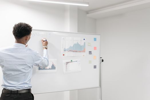 Man reviews COVID-19 data charts on whiteboard in office setting.