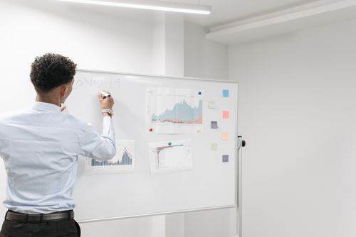 Free Man reviews COVID-19 data charts on whiteboard in office setting. Stock Photo