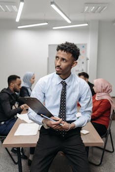 Diverse business team engaged in a meeting, with a man holding a clipboard in a modern office.