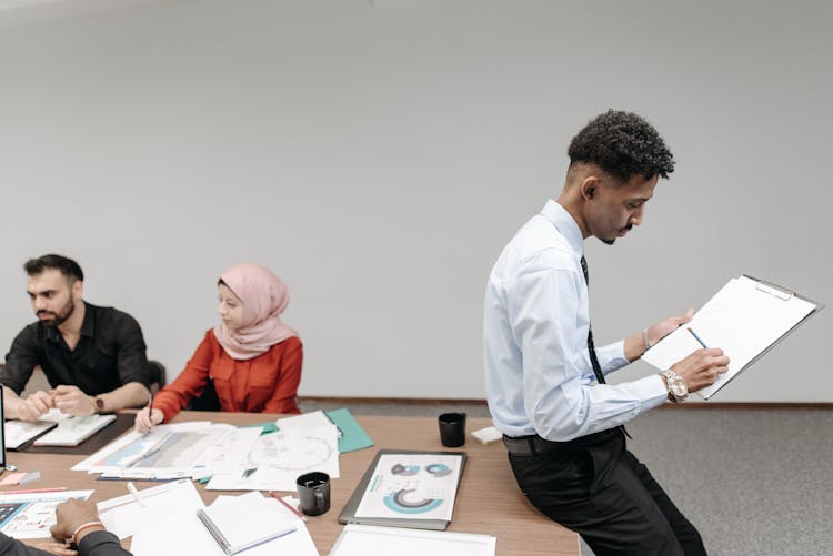 A Man In Corporate Attire Sitting On A Table While Holding A Clipboard