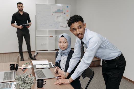 Team discussing business strategies in an office with laptops and whiteboard.