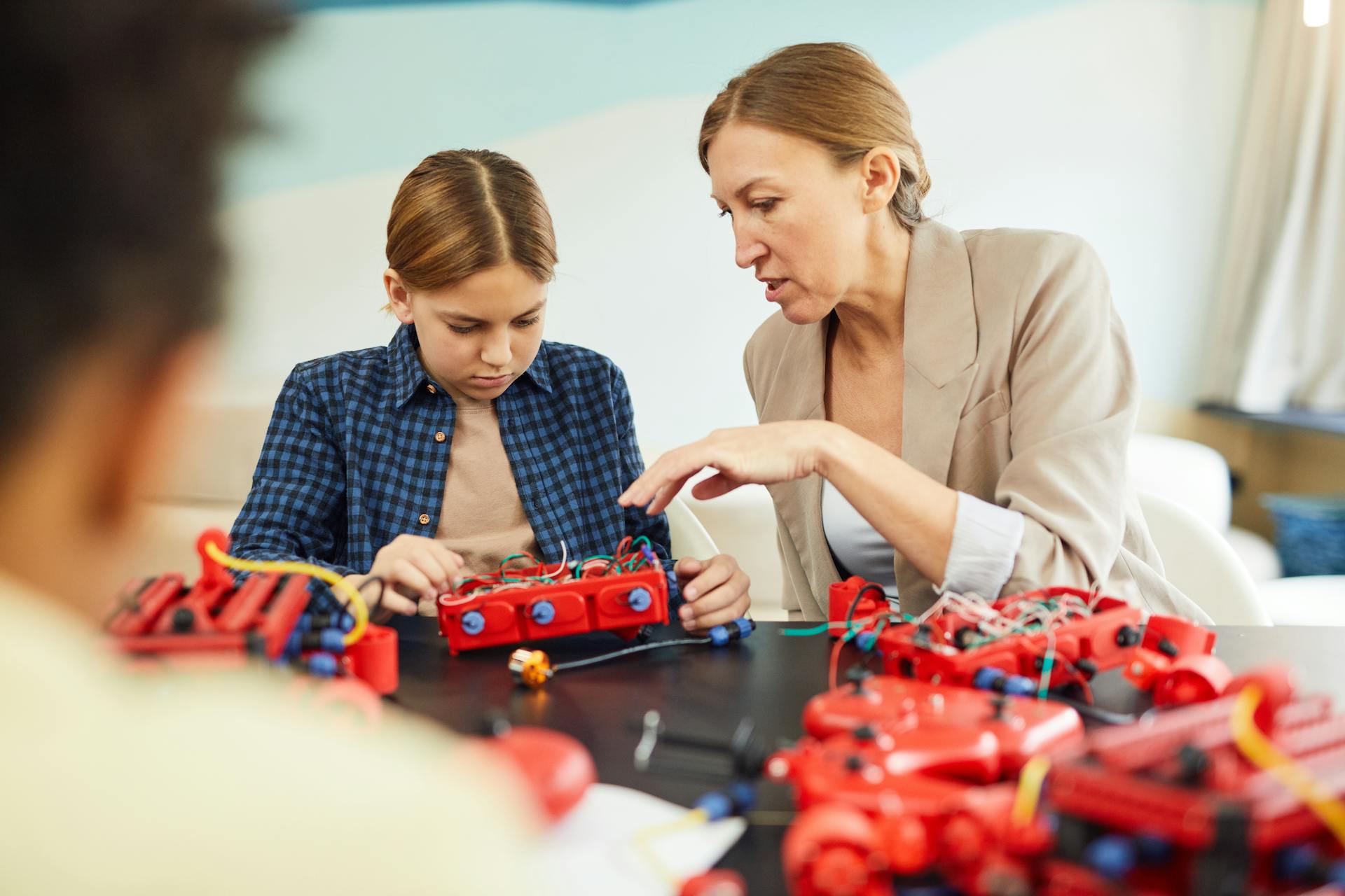 A woman educator helps a young student with a robotics project in a technology classroom.