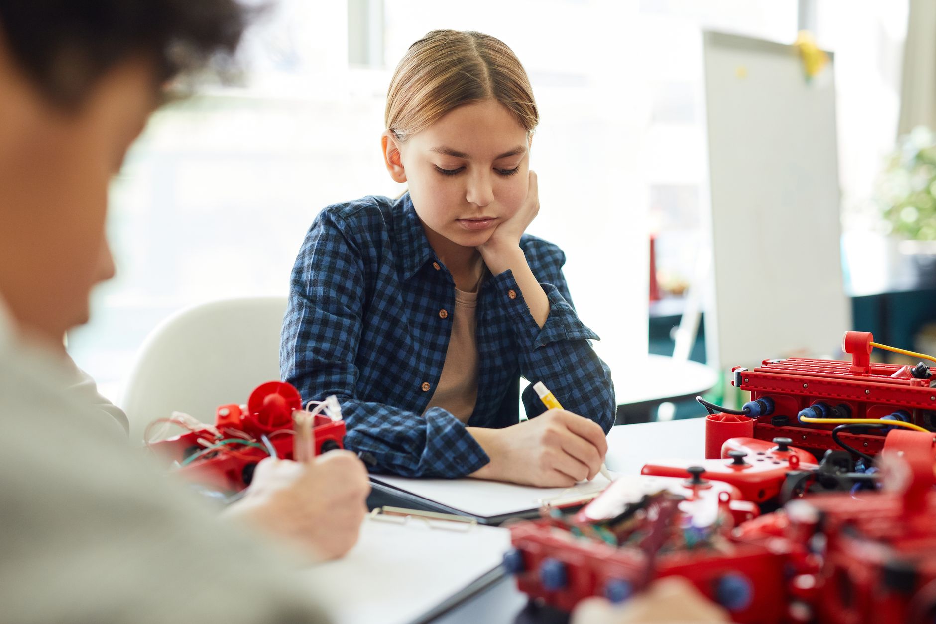 Teen girl concentrating on a robotics project, showcasing STEM education in a classroom setting.