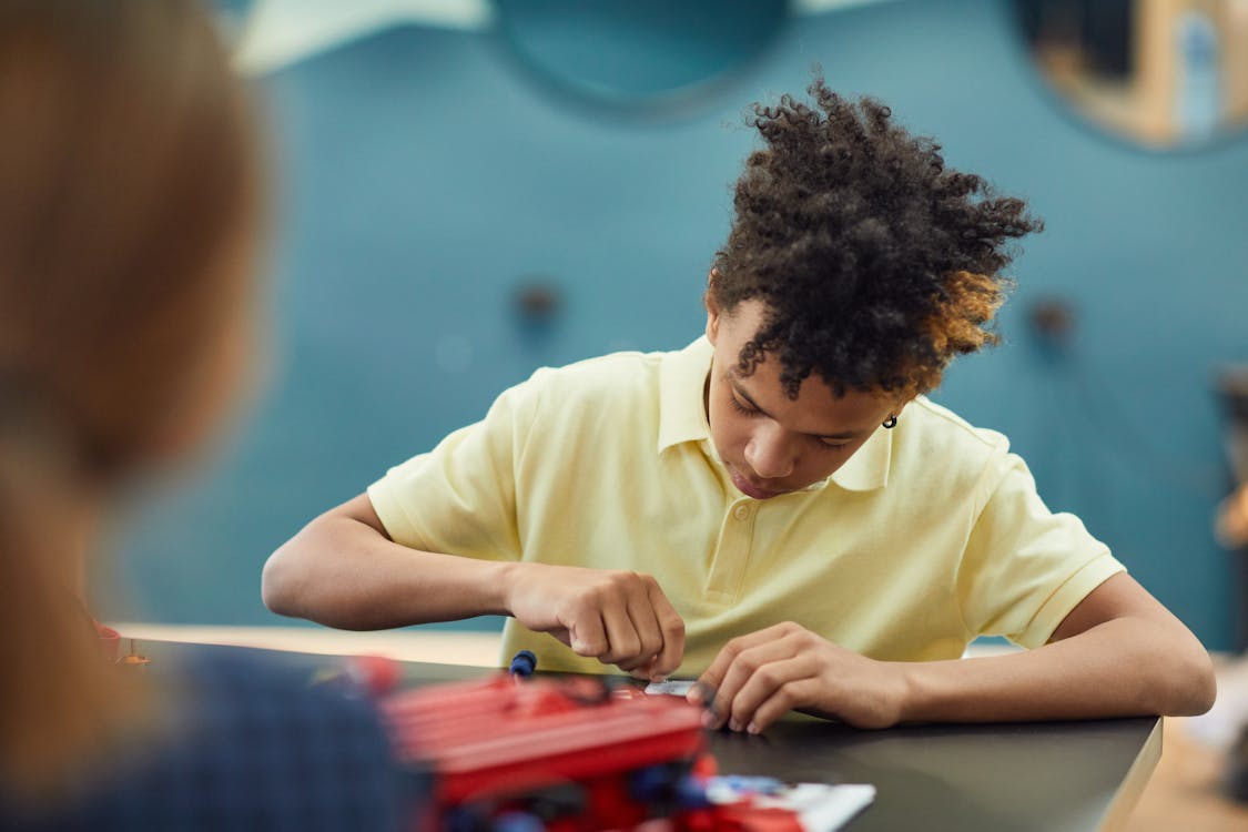 Concentrated black male kid in casual wear sitting at table and creating new project in light room