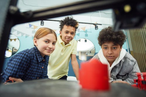 Free Low angle of cheerful group of multiracial children sitting together and observing work of 3D printer in light workshop Stock Photo