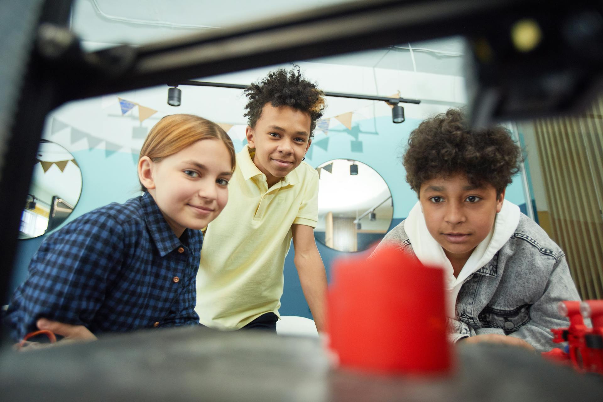 Low angle of cheerful group of multiracial children sitting together and observing work of 3D printer in light workshop