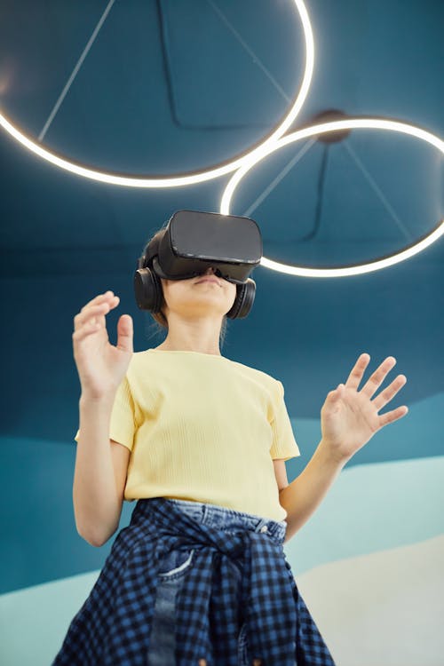 Free From below of anonymous girl standing with hands raised while experiencing virtual reality in studio Stock Photo