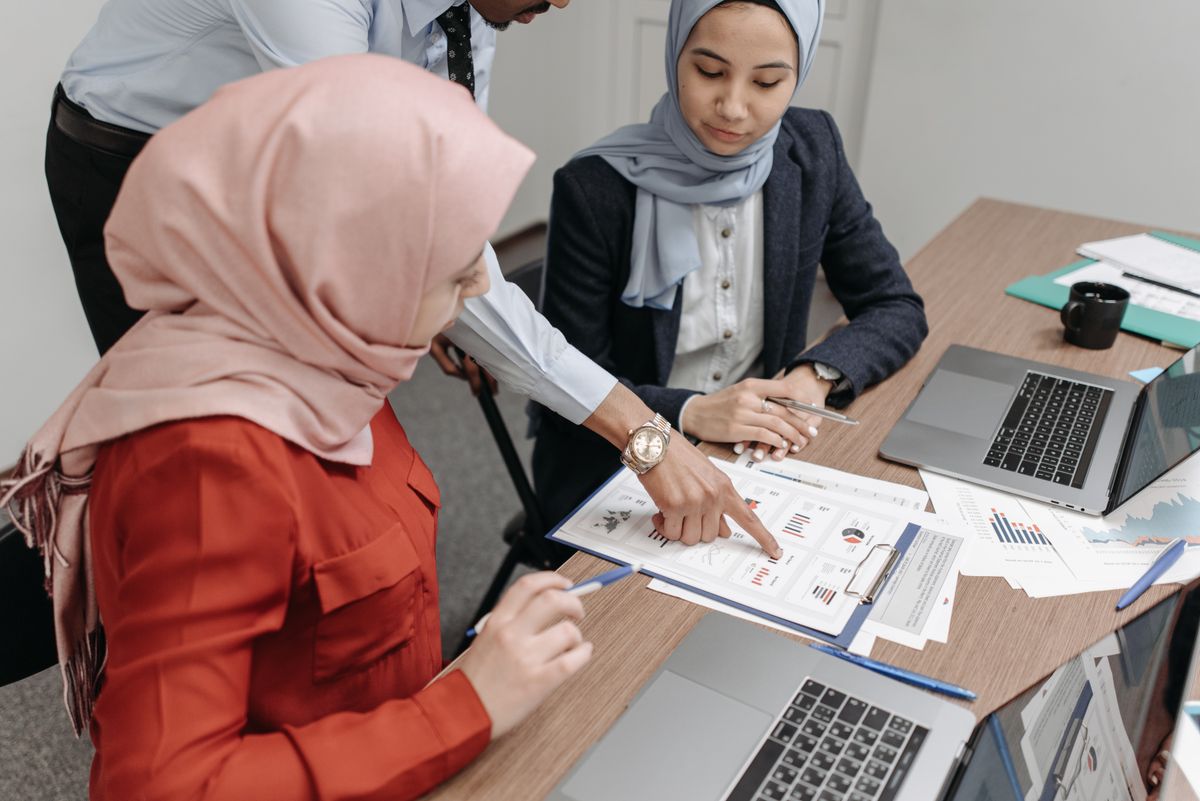 Team of women in hijabs reviewing documents and data with a colleague