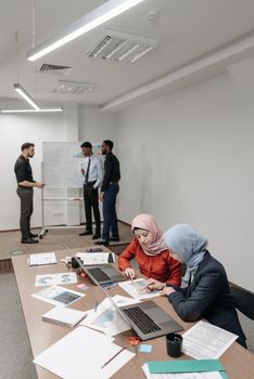 A diverse team collaborates around a table with laptops in an office setting.