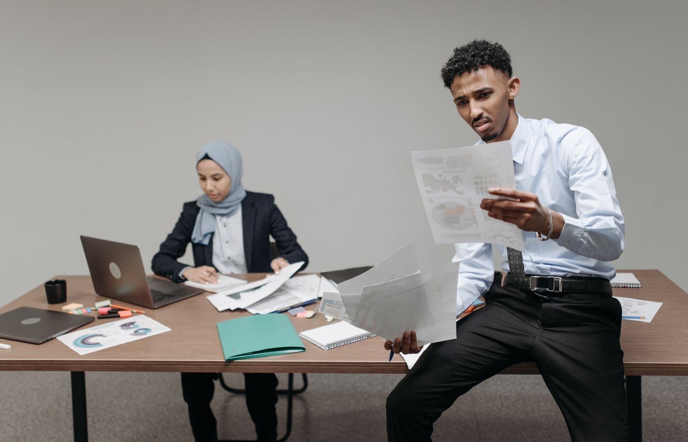 African American man and hijabi woman reviewing reports and documents in an office environment, showcasing teamwork.