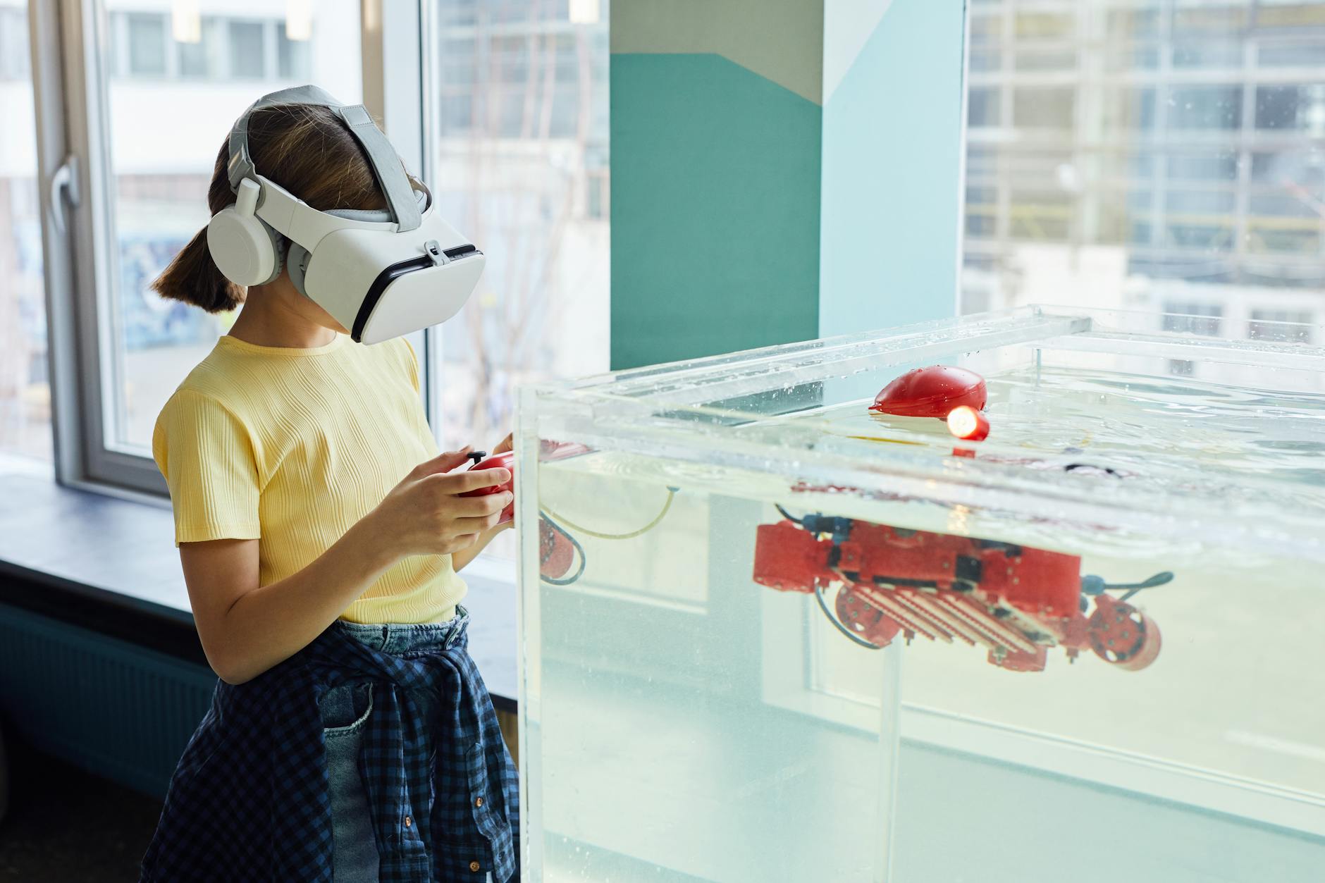 Vista lateral de una niña con gafas VR y explorando un nuevo robot con controladores en una sala de luz