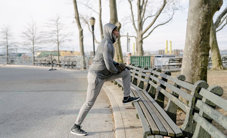 Old Black Man In Sportswear Stretching Legs In Park