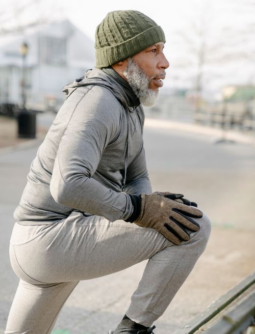 Free Side view of aged gray haired African American male in sportswear stretching legs while warming up before training and looking away in city park Stock Photo
