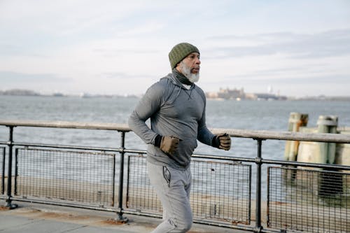 Free Side view of bearded senior African American male athlete in sportswear running along seafront on embankment in morning and looking away Stock Photo