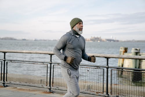 Side view of bearded senior African American male athlete in sportswear running along seafront on embankment in morning and looking away