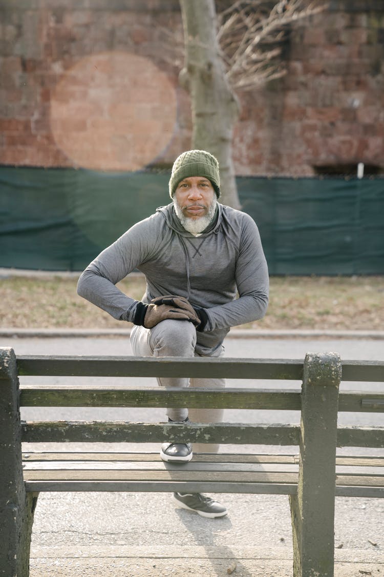 Focused Old Black Man Stretching Legs On Bench