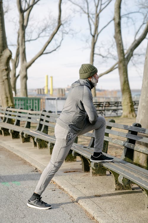 Free Side view of aged African American male athlete in activewear warming up on wooden bench in park in autumn morning Stock Photo