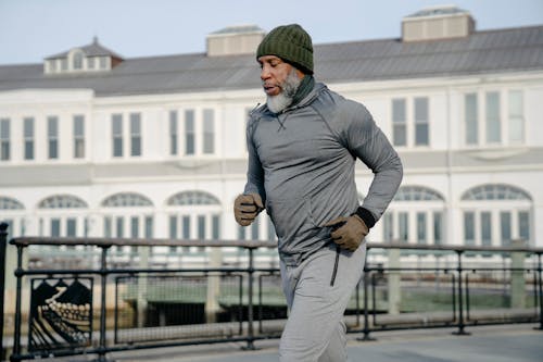 Free Concentrated African American bearded aged male athlete with closed eyes in activewear running on city street in sunny day Stock Photo